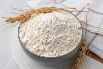 Wheat flour and spikes on white table, closeup