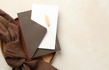 Blank invitation card, envelope, wooden tray, cloth and dry spike on beige background, top view....