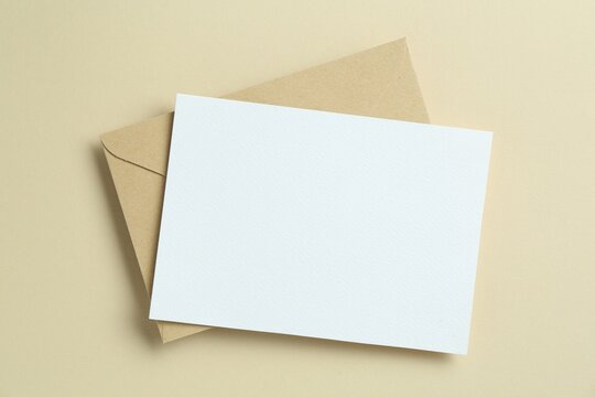 Blank invitation card and envelope on beige background, top view. Space for design