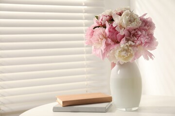 Bouquet of beautiful peonies in vase and books on white table indoors. Space for text