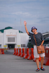 A cheerful woman waves joyfully in front of a building, wearing a bucket hat, casual clothes, and a...