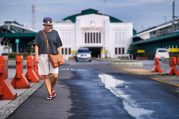A woman in casual clothes walks beside orange barriers on a wet street, looking down, a white building in the background