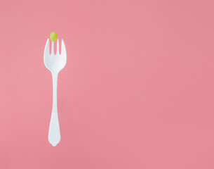 green grape on big white fork on pink background