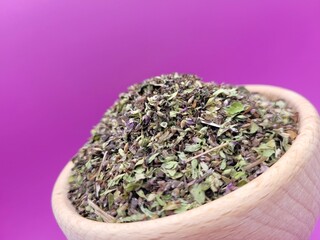 Dried pile of basil leaves on a violet background.