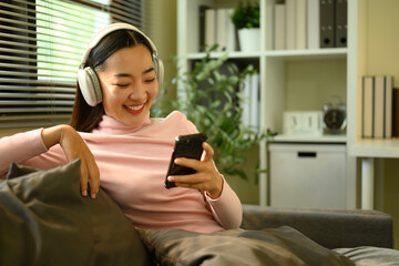 Casual indoor moment of an Asian woman enjoying music or podcasts through wireless headphones,...