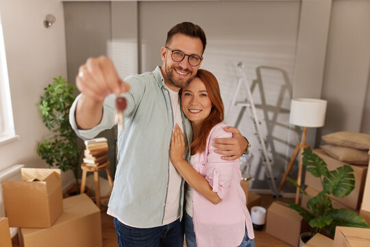 Excited couple embraces while showcasing keys to their new home, surrounded by unpacked boxes and signs of settling in, reflecting joy and new beginnings.