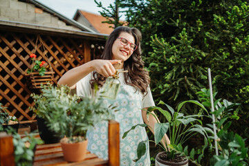 Young woman taking care of plants with water can and mister	
