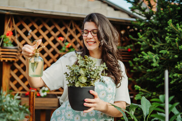 Young woman taking care of plants with water can and mister	

