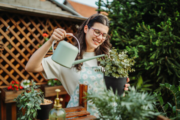 Young woman taking care of plants with water can and mister	
