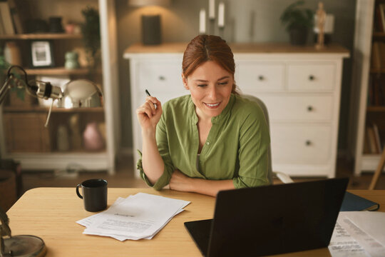 Smiling woman engages in a video call from her home office, surrounded by papers and a coffee cup, showcasing a warm and inviting workspace atmosphere.