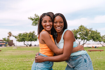 Obraz premium Two happy multiracial female friends embracing in a park during summer vacation