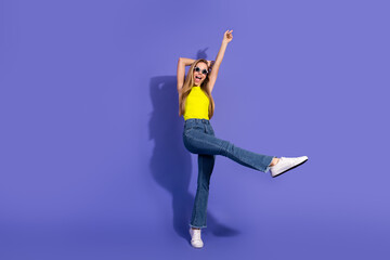Happy young woman in casual outfit dancing joyfully on a vibrant purple background while wearing...
