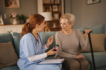 A home healthcare worker is explaining the medication instructions to an elderly woman while...