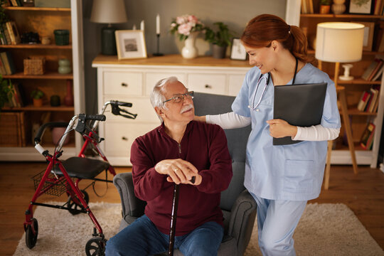 A young redhead female nurse, wearing a stethoscope, is comforting an elderly white male patient. The patient is sitting in an armchair while holding a cane. - Powered by Adobe