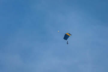 Skydiver with a blue and yellow parachute gliding through the air on a clear day
