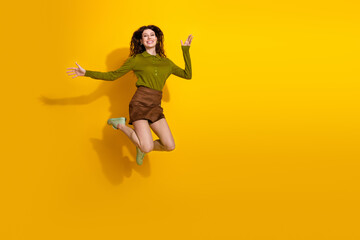 Obraz premium Cheerful young woman jumping with joy against a vivid yellow background, expressing happiness and energy in casual fashion