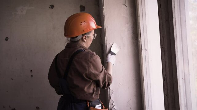 Female builder or repair worker removing old painted from wall. House renovation and renewal