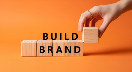 Wooden blocks spelling "Build Brand" on orange background A hand places the final block, showcasing brand building concept
