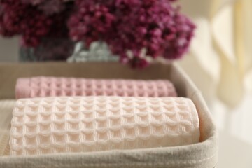 Clean waffle towels in basket and vase of lilac flowers, closeup