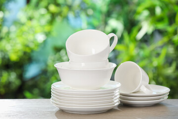 Different clean dishes on wooden table against blurred green background