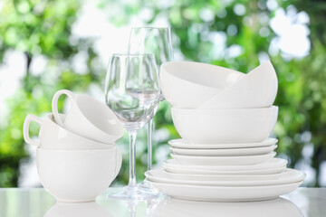 Different clean dishes on white table against blurred green background