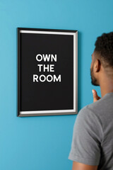 Man facing 'Own the Room' frame on blue wall