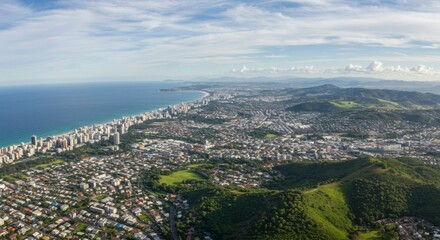 Fototapeta premium Panoramic aerial view of coastal city, showing a blend of urban development and natural landscape, including ocean, beach, and mountains under a partly cloudy sky