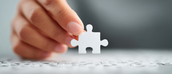 Assembling the last piece of a jigsaw puzzle a closeup of a hand fitting a blank white piece into a background frame for accomplishment and completion strategy