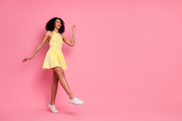 Joyful young woman in a yellow dress against a pink background expressing happiness and carefree...