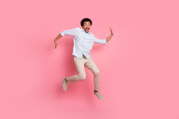 Energetic young man in casual attire jumping with excitement against a vibrant pink background...