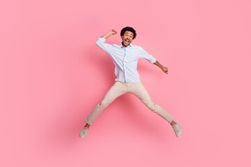 Excited young man jumping against a pink background radiating happiness and energy in casual attire