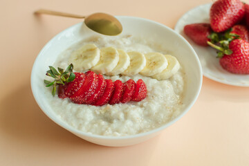 gluten-free porridge with banana and ripe red strawberries on a plate on a light background. free space for text. healthy eating. a healthy snack. horizontal photo.