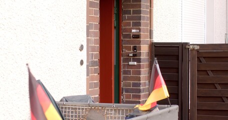 The image shows a residential entrance adorned with vibrant German flags, indicating a joyful...