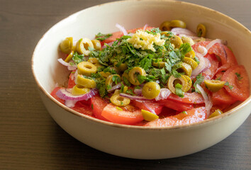 Fresh and simple summer tomato salad in a bowl. Close-up image of juicy red tomatoes with herbs,...