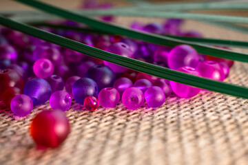 A scattering of vibrant purple beads on a rustic burlap texture, with green accents. Perfect for...