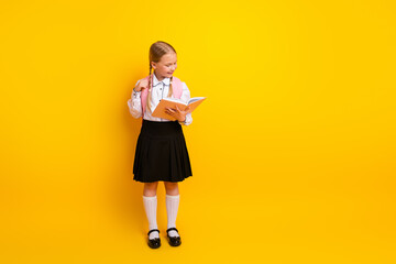 Young schoolgirl in a stylish uniform holding a book against yellow background, representing...