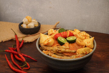 Traditional spicy Indonesian street food called seblak, served with chicken feet, tofu, noodles, chili, and lime in a ceramic bowl. Popular Sundanese dish.
