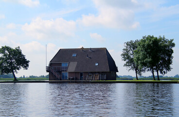 House and trees at a lake against blue sky with white clouds (Giethoorn, Netherlands)