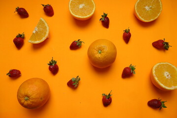 Flat lay of fresh strawberries and halved oranges on a vibrant orange background, creating a bold...