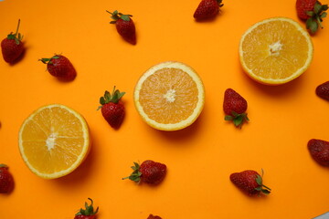 Flat lay of fresh strawberries and halved oranges on a vibrant orange background, creating a bold...