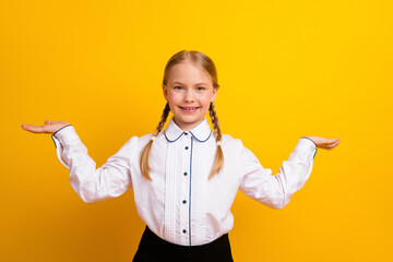Smiling young girl in white school uniform gesturing with hands against a yellow background promoting back-to-school theme