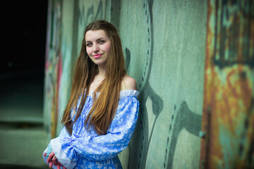 Fototapeta premium Young woman in blue dress posing near urban graffiti wall at night