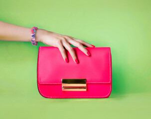 Beautiful woman hand with bracelet touching the leather luxury pink bag purse isolated on green background. 