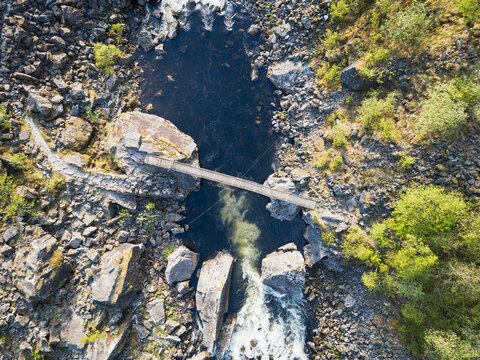 Fototapeta Top down aerial drone view of a footbridge crossing a river canyon next to a waterfall in Norway.