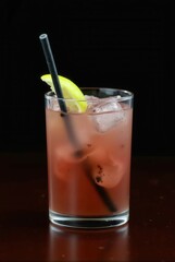 Crimson Cocktail: A refreshing crimson cocktail glistens in a glass filled with ice, garnished with a lime and black straw, capturing the essence of a perfect beverage.