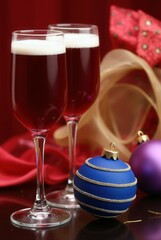 Festive Cheers: Two elegant champagne flutes filled with a ruby-red liquid, set against a backdrop of holiday ornaments and decorations, evoking warmth and celebratory mood.