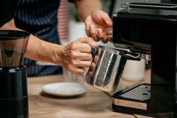 A young Asian male barista, dressed in a striped apron, skillfully creates beautiful latte art in a cozy, modern cafe, professional coffee equipment and takeaway cups.