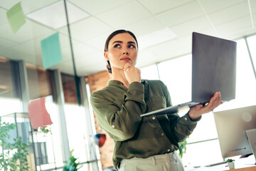 Thoughtful businesswoman holding laptop in a professional modern office space considering ideas for a corporate project