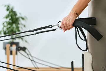 Fitness, pilates and reformer exercise. Young strong  woman in modern studio training with straps in her hands, closeup. 
