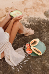 Two women sit side by side on warm rocks with a plate of sliced papaya, melon and citrus. Shared...